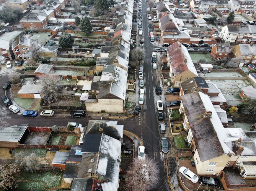 An aerial view of a narrow residential street in Hounslow showing closely packed terraced houses with pitched roofs, some of which have snow on top. Cars are parked along both sides of the street, wit